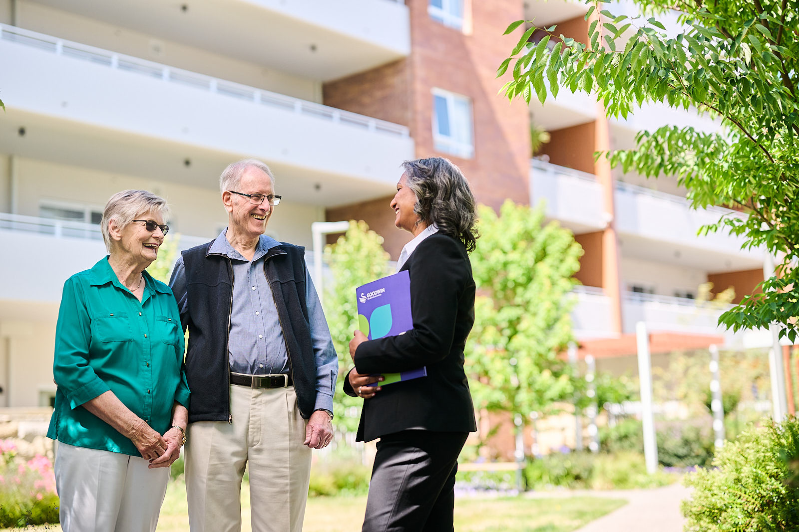 Couple speaking with a Goodwin team member outside a retirement living apartment building.